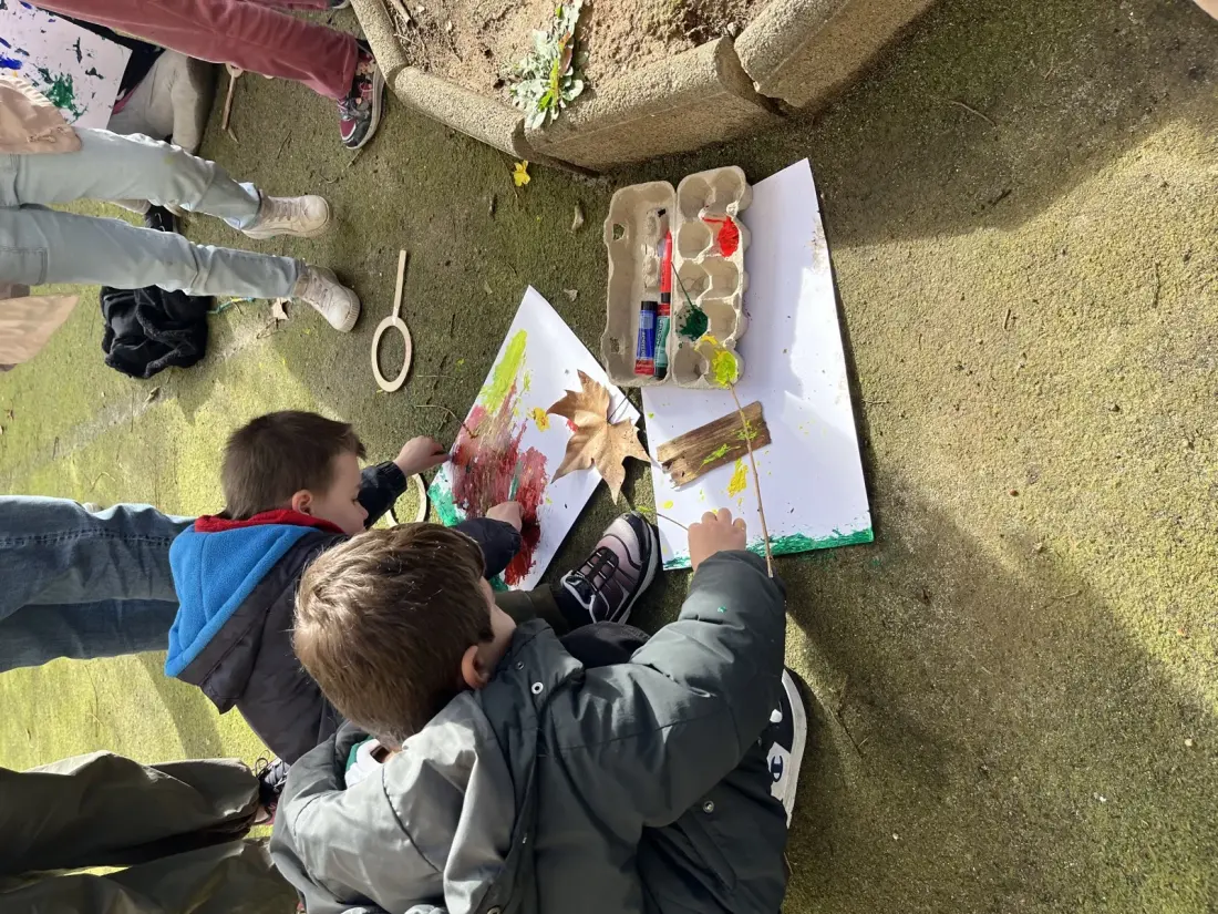 Two children painting with leaves and twigs in a schoolyard
