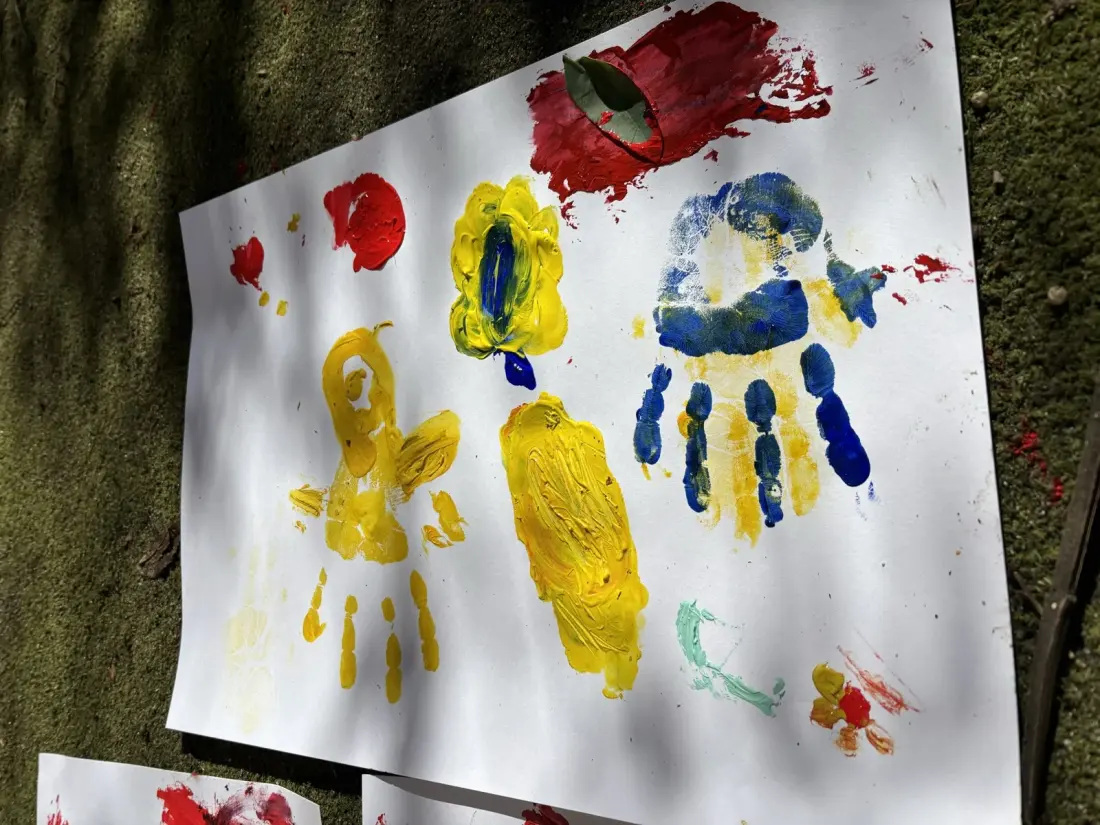 Children's painted handprints in yellow, red and blue on white paper